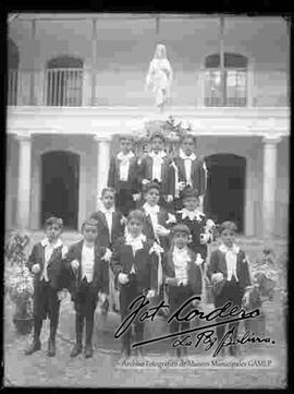 Grupo de niños en el día de su primera comunión,  agarrando rosarios y posando delante de una fuente con la imagen de cristo