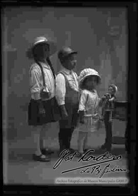 Foto de estudio de tres niños. Una niña y dos niños, la mas pequeña sujeta una muñeca