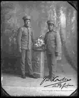 Foto de estudio de dos soldados, apoyados a una pequeña columna con un jarrón de flores