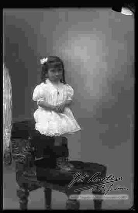 Foto de estudio de una niña que se encuentra parada encima de un sillón