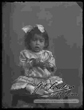 Foto de estudio de una niña pequeña que se encuentra sentada en un banquito