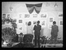 Tres personas observando la exposición de fotografías "Foto Cordero Jiménez", en el salón de la cancillería. octubre 1948.