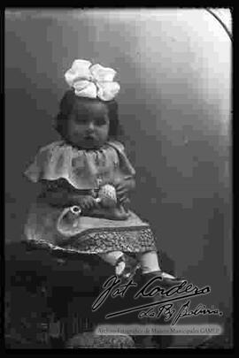 Foto de estudio de una niña pequeña, sentada en la cabecera de un sillón