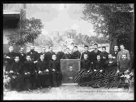 Grupo de curas y profesores posando delante la virgen María Auxiliadora, sosteniendo un cuadro del padre Don Bosco