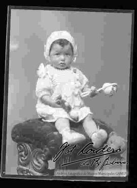 Foto de estudio de una niña pequeña sentada en la cabecera de un sillón, sosteniendo en sus manos unos juguetes