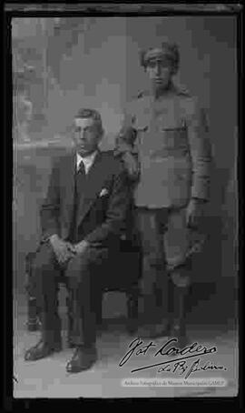 Foto de estudio de un soldado de la Guerra del Chaco junto a su padre, que se encuentra sentado a su lado en un sillón