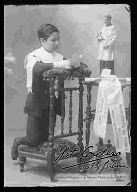 Foto de estudio del niño david h. baldivieso,  el día de su primera comunión, junto a una imagen religiosa