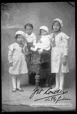 Foto de estudio de cuatro niños (hermanitos). tres niñas y un niño junto y encima de un sillón