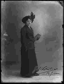Fotografía de estudio de una dama, luciendo un traje, sombrero y cartera.