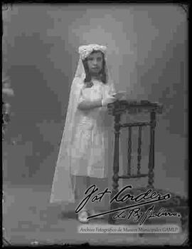 Foto de estudio de una niña, e l día de su primera comunión, apoyada a una silla