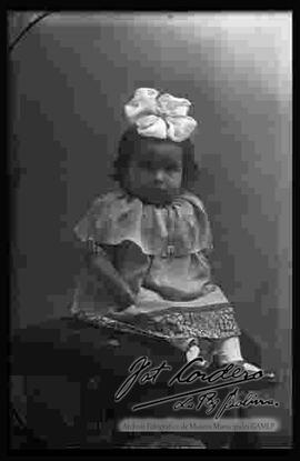 Foto de estudio de una niña pequeña, sentada en la cabecera de un sillón