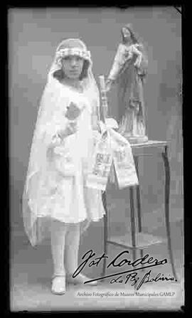 Foto de estudio de la niña Maruja Zaballa, parada junto a una imagen religiosa, el día de su primera comunión