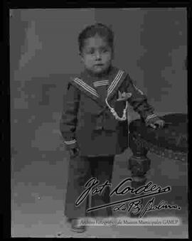 Foto de estudio de un niño pequeño, parado junto a un sillón