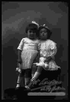 Foto de estudio de dos niñas que se encuentran encima de un sillón. Una parada y la otra sentada en la cabecera