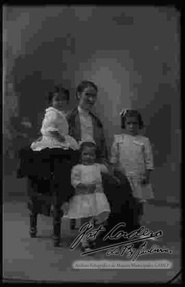 Una madre sentada en un sillón junto a sus tres hijas pequeñas,  foto de estudio de la familia.