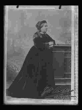 Reproducción de la imagen de una dama de perfil, que lleva puesto: Un vestido largo y oscuro.