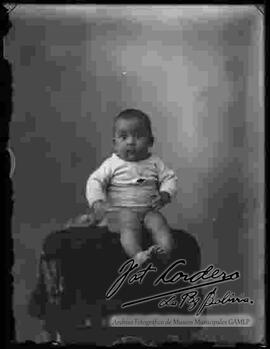 Foto de estudio de un bebe sentado en la cabecera de un sillón