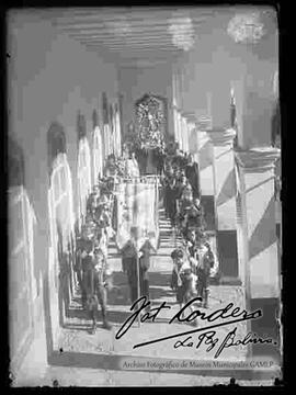 Procesión de la imagen de un santo, por parte de estudiantes varones junto a curas y profesores, por los pasillos de los salones de clases de un colegio