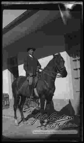 Un varón de traje y sombrero, montado a caballo en el patio de una casa