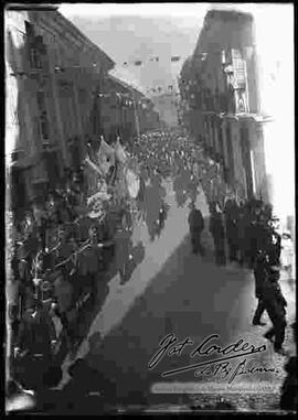 Desfile cívico por el 16 de julio, donde se puede apreciar  una carrosa alegórica con el busto de Pedro Domingo Murillo, tirado por caballos y con la presencia de autoridades de gobierno como ser el presidente Ismael Montes, por la calle Mercado.