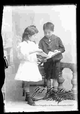 Foto de estudio de dos niños (hermanitos). Una niña y un niño observando una revista