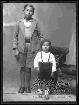 Foto de estudio de dos niños parados junto a un sillón