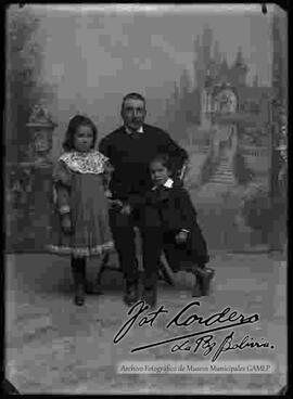 Foto de estudio de un padre sentado en un sillón junto a sus dos hijas pequeñas