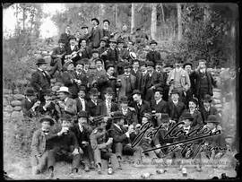 Grupo de varones y algunos militares, compartiendo bebidas en un día de campo