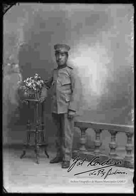 Foto de estudio de un soldado que se encuentra parado a lado de un barandal y  una mesita con flores