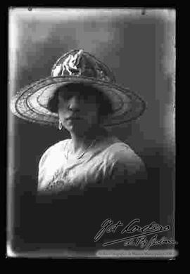 Foto de estudio de medio cuerpo de una dama que lleva puesto un modelo de sombrero con adorno.