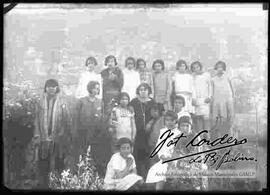 Imagen de un grupo de señoritas que se encuentran en un jardín rodeando a una señora  (Posiblemente sean estudiantes y la profesora de algún establecimiento)