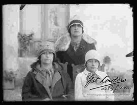 Dos damas y un señorita en el patio de una casa. Presentan tres tipos de sombrero en forma de gorro.