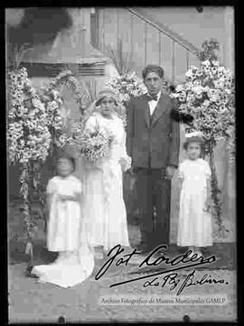 Novios junto a dos niñas y delante de arreglos florales, en el patio de una casa particular, el día de su matrimonio