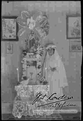 Dama junto a un altar de una imagen religiosa, en el día de su primera comunión