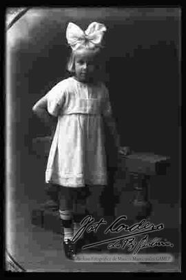Foto de estudio de una niña rubia, parada junto a una baranda