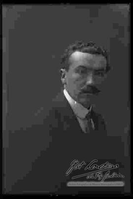 Foto de estudio con esfumador de un varón de bigote que viste de traje.