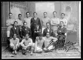 Foto de estudio de un equipo de futbol, junto a sus dirigentes sosteniendo una copa