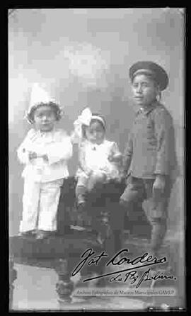 Foto de estudio de dos niños y una niña (hermanitos). Uno de los niños se encuentra disfrazado de payasito