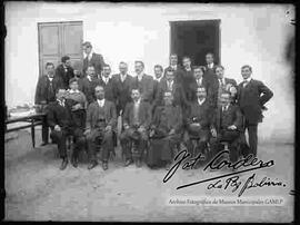 Grupo de varones junto a un cura y reunidos en el patio de una casa particular