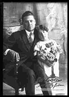 Reproducción de la fotografía de un varón que se encuentra sentado en una silla junto a su hija.