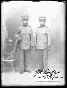 Foto de estudio de dos  Militares: Uno con la mano en una silla de mimbre