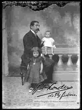 Foto de estudio de un padre sentado en un banquito junto a sus dos hijas pequeñas