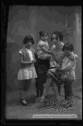 Foto de estudio de una familia. Una dama sentada en un sillón junto a sus tres hijos