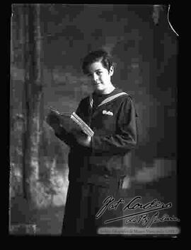 Foto de estudio de una joven señorita que sostiene un libro en las manos y viste con un uniforme con cuello de marinero.