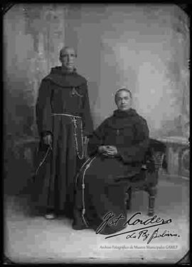 Foto de estudio de dos sacerdotes franciscanos extranjeros, uno parado y el otro sentado en una silla tallada